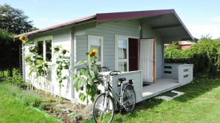 Small grey cabin with a bicycle in front and sunflowers beside the garden at At słonecznikiem, sunny day.