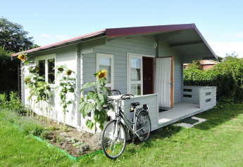 Pequeña cabaña gris con bicicleta al frente y girasoles en el jardín en At słonecznikiem, día soleado.