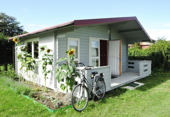 Kleine grijze chalet met een fiets vooraan en zonnebloemen bij de tuin bij At słonecznikiem, blauwe lucht.