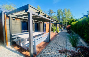 Vue extérieure d'une cabane glamping moderne avec terrasse couverte, banc et allée paysagée.