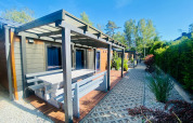 Vue extérieure d'une cabane glamping moderne avec terrasse couverte, banc et allée paysagée.