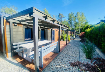 Buitenaanzicht van een moderne glamping hut met overdekt terras, picknickbank en tuinpad.