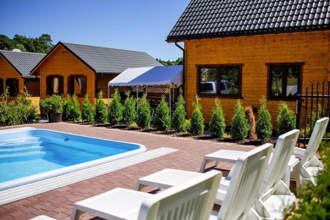 Outdoor pool with white loungers in front of wooden lodges at Holiday resort with the pool Wiselka-35 sqm Type A.