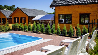 Außenpool mit weißen Liegestühlen vor Holzhütten im Holiday Resort mit Pool Wiselka-35 qm Typ A.