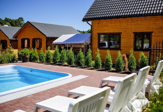 Outdoor pool with white loungers in front of wooden lodges at Holiday resort with the pool Wiselka-35 sqm Type A.