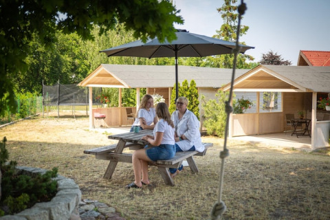 Drie mensen zitten aan een picknicktafel met parasol bij vakantiehuisjes in Miedzyzdroje, Duitsland.