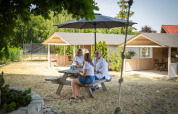 Drie personen zitten aan een picknicktafel onder een parasol bij vakantiehuisjes in Miedzyzdroje.