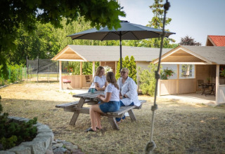 Drie personen zitten aan een picknicktafel onder een parasol bij vakantiehuisjes in Miedzyzdroje.
