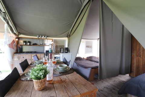 Interior view of a safari tent featuring a dining table, kitchen, and separate sleeping areas with beds.