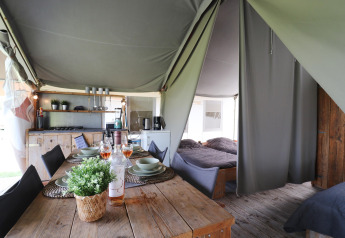 Interior view of a safari tent featuring a dining table, kitchen, and separate sleeping areas with beds.