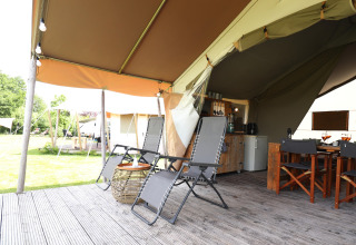 Terrasse de tente safari avec chaises longues, coin repas et vue sur la pelouse, ambiance glamping relaxante.