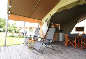 Safari tent porch with reclining chairs, dining set, and open view of the grassy site, perfect for glamping.