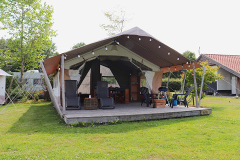 Tente safari avec terrasse en bois et mobilier de jardin, entourée de pelouse et d’arbres verdoyants.