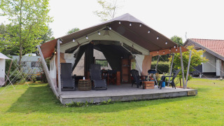 Tente safari avec terrasse en bois et mobilier de jardin, entourée de pelouse et d’arbres verdoyants.