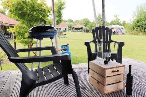 Outdoor seating at Safari tent 'Noflik' in the Netherlands with a grill, chairs, and wooden table.
