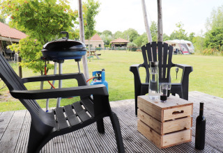 Coin salon extérieur du safari-tente « Noflik » aux Pays-Bas avec barbecue, chaises et table en bois.