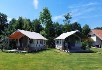 Two safari tents set up on a well-kept green lawn, surrounded by trees and under a clear blue sky.