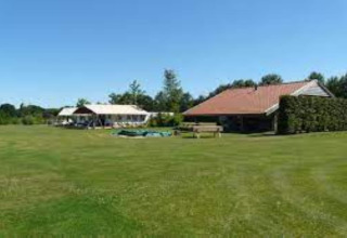 Foto einer Glamping-Unterkunft mit Zelt und Haus auf einer weitläufigen grünen Wiese bei Sonne.