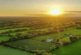 Vue aérienne d'un hébergement glamping à la campagne entouré de champs verts au coucher du soleil.