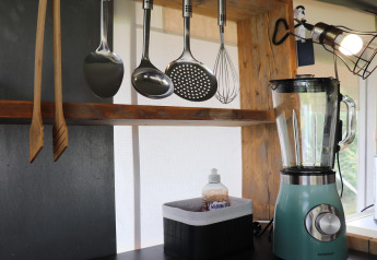Kitchen inside a safari tent featuring hanging utensils, a teal blender, dish soap, and natural lighting.