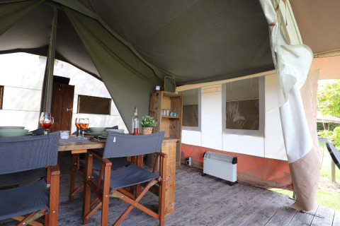 Intérieur d’une tente safari avec table à manger, chaises, étagère en bois et chauffage sur sol en bois.