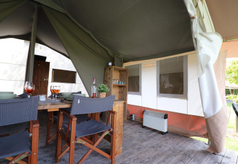 Indretning af en safari-telt med spisebord, stole, træhylder og varmeapparat på trægulv.