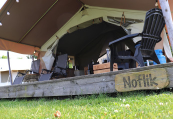 Safari tent with lounge chairs and a wooden sign that reads 'Noflik' on the deck in the foreground.