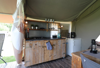 Kitchen area in Safari tent 'Noflik' in the Netherlands featuring wooden cabinets, stove, and fridge.