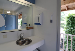 Salle de bain moderne au glamping avec lavabo, miroir, distributeur de savon et vue sur la verdure.