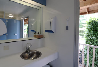 Moderne badeværelse på glamping med vask, spejl, sæbedispenser og udsigt til frodigt udendørsområde.