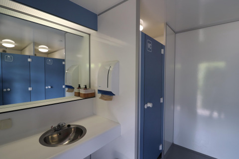 Photo of modern restroom facilities with a mirror, sink, and blue stalls at a glamping accommodation.