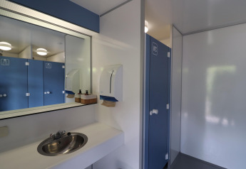 Foto de instalaciones modernas de baño con espejo, lavabo y cabinas azules en alojamiento glamping.