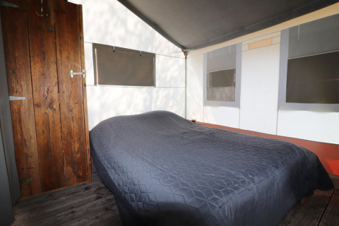 Interior of a safari tent featuring a double bed, a wooden door, and windows with blackout shades.