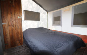 Interior of a safari tent featuring a double bed, a wooden door, and windows with blackout shades.