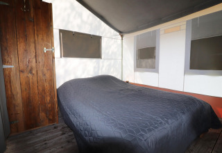 Intérieur d’une tente safari avec lit double, porte en bois et fenêtres munies de stores occultants.
