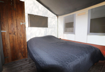 Interior of a safari tent featuring a double bed, a wooden door, and windows with blackout shades.