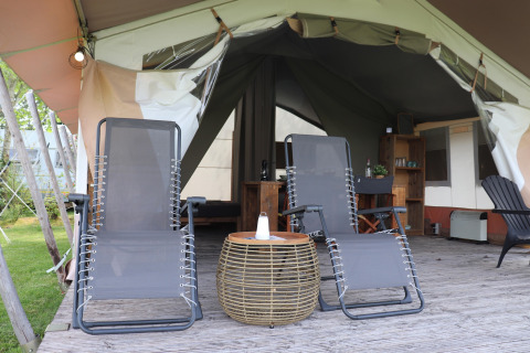 Two lounge chairs on a wooden deck outside safari tent 'Noflik', featuring cozy furnishings in the Netherlands.