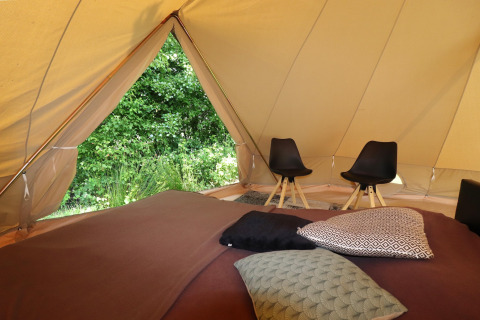 Interno di una tenda glamping con cuscini comodi, sedie e vista panoramica sulla natura verde fuori.