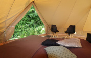Indvendigt syn af et glamping-telt med komfortable puder, stole og udsigt til grøn natur udenfor.