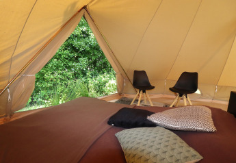Interior de una tienda glamping con cojines cómodos, sillas y vistas panorámicas a la naturaleza verde.