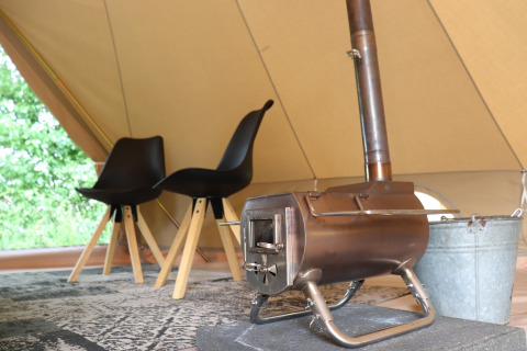 Indretning af glamping-telt med to sorte stole, et tæppe og en lille brændeovn på måtten.