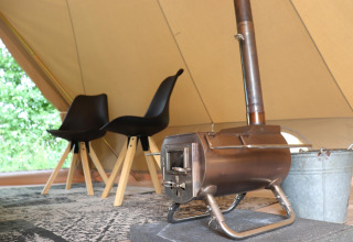 Interior de tienda glamping con dos sillas negras modernas, alfombra decorativa y pequeña estufa de leña.