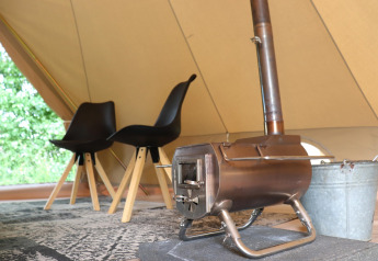 Indretning af glamping-telt med to sorte stole, et tæppe og en lille brændeovn på måtten.