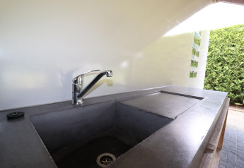 Évier de cuisine extérieur avec robinet moderne dans un hébergement glamping, haie verte en arrière-plan.