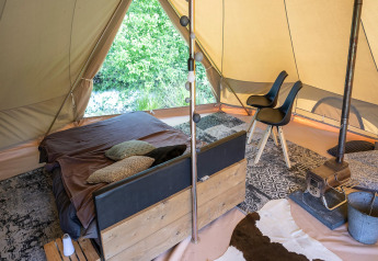 Interno di una tenda glamping con letto, sedie, tappeti e stufa a legna immersi nella natura.