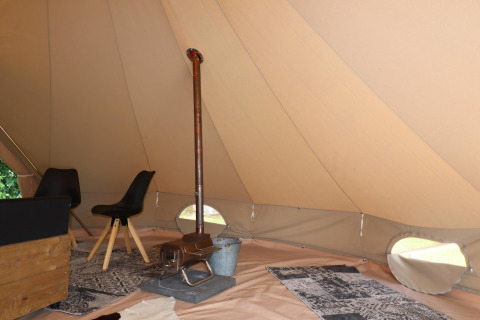 Interior de una tienda glamping con estufa de leña, sillas negras y alfombras decorativas en el suelo.
