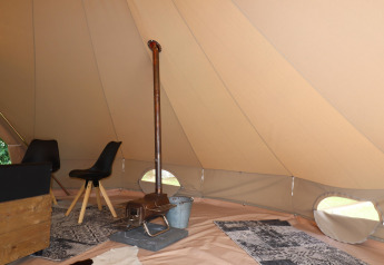 Interno di una tenda glamping con stufa a legna, sedie nere e tappeti decorativi sul pavimento.