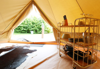 Inside a glamping tent with a kitchen cart, dishes, and a cowhide rug, facing green trees outside the entrance.
