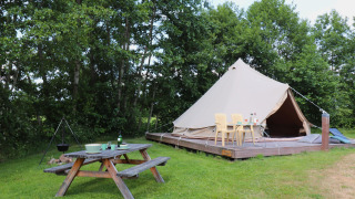 Et stort telt på en træplatform med borde, stole og picnicbord midt i grønne omgivelser ved glamping.