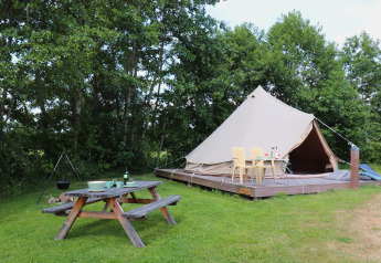 Grande tenda su piattaforma in legno con tavolo da picnic e sedie in un ambiente glamping all’aperto.